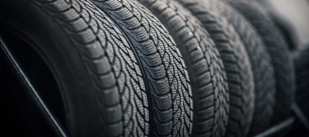 Close-up of several black car tires lined up side by side, their intricate tread patterns sharply lit against a dark background, conveying a rugged, industrial mood.