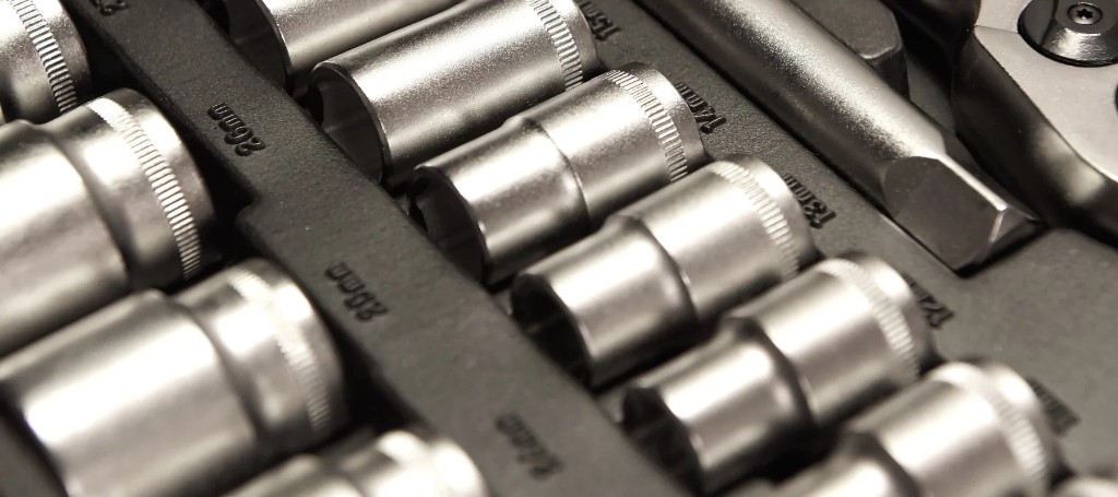 Close-up of polished chrome socket wrench attachments arranged in a black tool tray, their reflective surfaces creating a precise, orderly workshop feel.