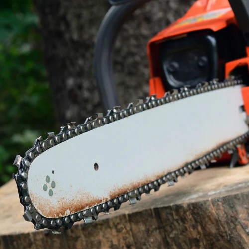 Close-up of an orange chainsaw resting on a log, its sharp metal chain and guide bar in focus against a blurred forest backdrop; rugged, practical tone.